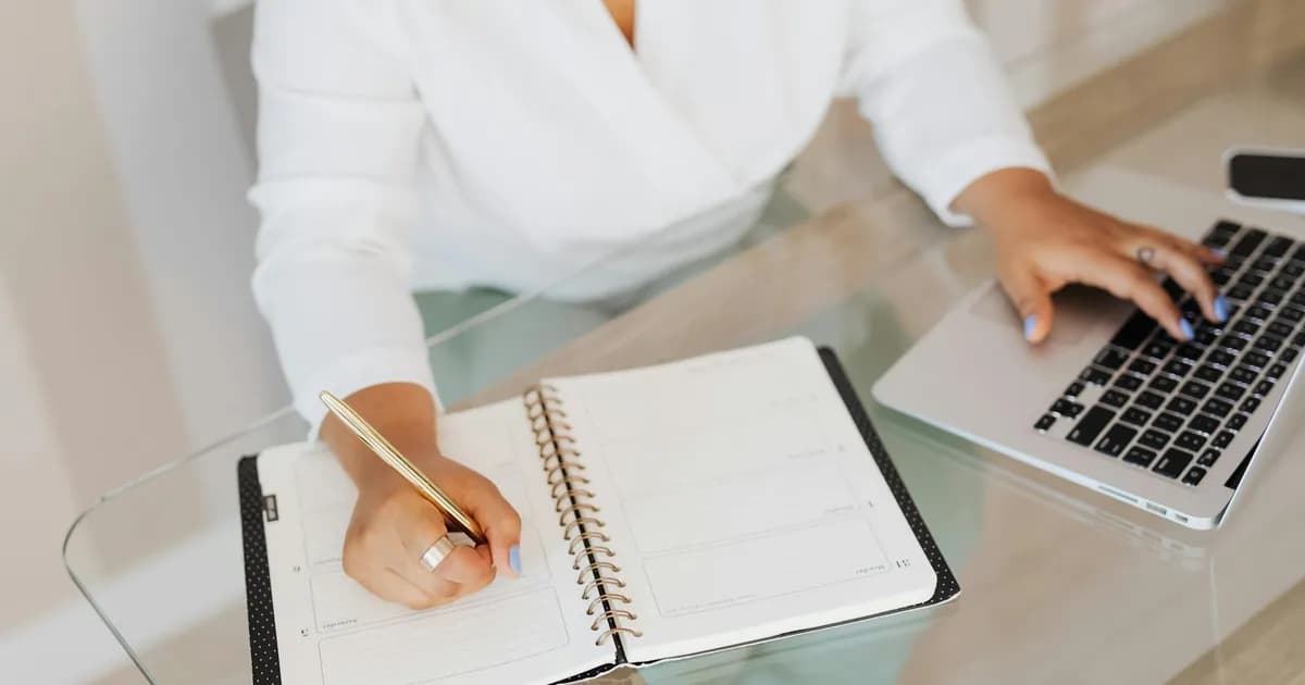 Personne rédigeant des textes de copywriting sur un carnet à côté d'un ordinateur portable