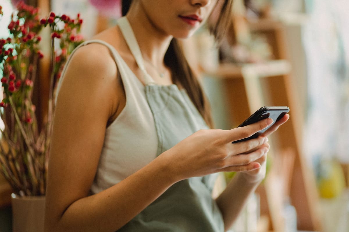 commerçante en tablier consultant son téléphone dans sa boutique de fleurs